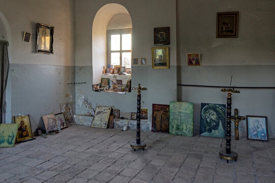 Wide shot of the simple interior of an Orthodox church in Sighnaghi, Kakheti region, Georgia, displaying various religious icons, paintings of Jesus Christ, tall metal candlesticks, and stone tile flo
