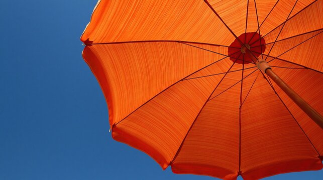 Low angle view of open bright orange beach umbrella against clear deep blue summer sky showing vibrant summer vacation and sunny outdoor relaxation