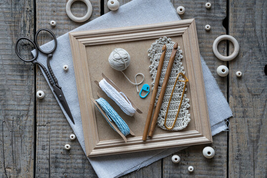 Rustic handmade craft flat lay with wooden crochet hooks decorative cords tassels wooden beads scissors and textile accessories arranged on wooden frame background top view
