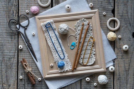 Creative handmade textile flat lay with blue decorative cord wooden crochet hooks tassels wooden beads scissors and craft accessories arranged on rustic wooden frame background