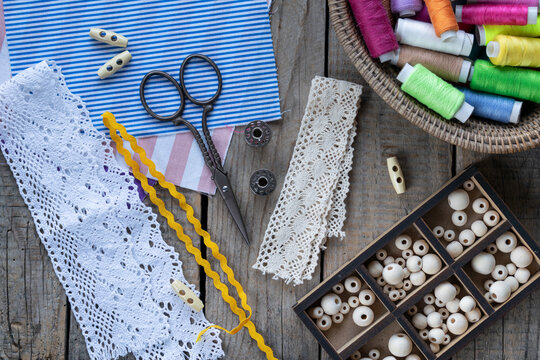Rustic sewing and handmade craft flat lay with lace fabric colorful threads scissors buttons beads and crochet accessories on wooden background with copy space