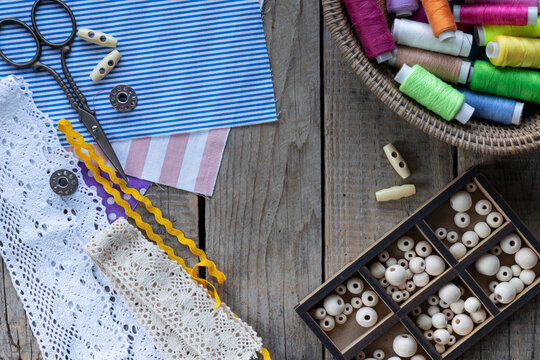 Rustic handmade sewing and textile craft composition with lace colorful threads scissors buttons beads and copy space on wooden background flat lay style