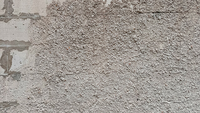 Rough grey spattered cement plaster texture on a building wall with a glimpse of lightweight concrete block.