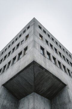 View of a concrete brutalist building taken from below showing the angular design and window patterns against an overcast sky at a city location in the late afternoon