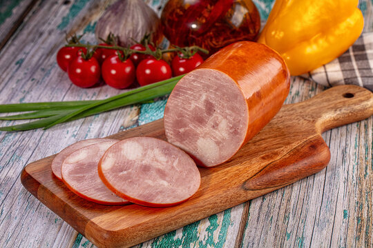 Sliced boiled sausage and fresh vegetables on wooden cutting board
