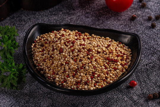 Raw tricolor quinoa in black bowl on dark textured background