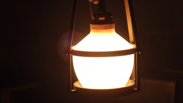 Vintage style glowing oil lantern with warm orange light shining in a dark atmosphere, rustic antique lamp providing soft illumination in a moody and atmospheric nocturnal setting