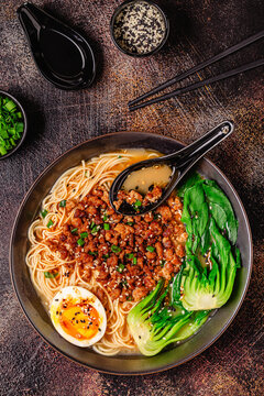 A bowl of noodles with minced meat, egg, and bok choy.