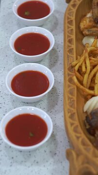 Slow motion camera panning of red tomato dipping sauces in small white bowls next to a traditional meat platter, vertical video.