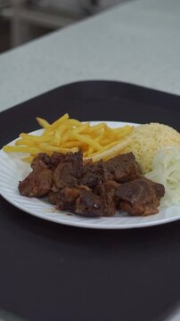 Slow motion camera panning of traditional roasted beef meat served with crispy french fries and sliced raw onions on a white plate, vertical video.