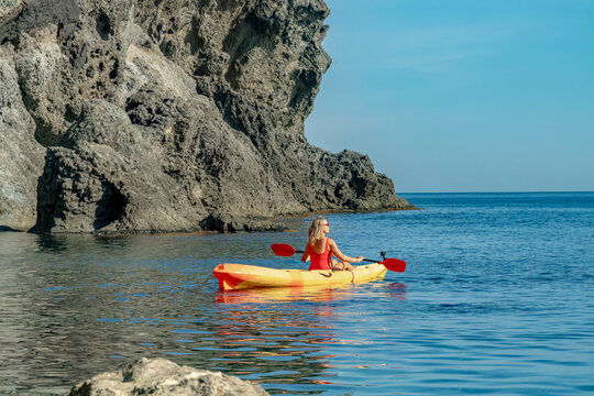 Woman kayaking sea, enjoying a peaceful summer day along a rugged rocky cliff coastline under clear blue sky