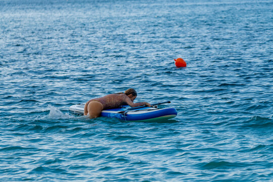 Paddleboarding woman ocean, a person attempts to get on her stand up paddleboard during summer recreation