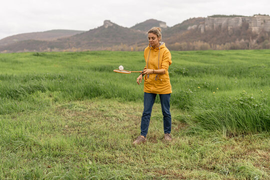 Woman playing badminton outdoors in green field with rocky mountain backdrop