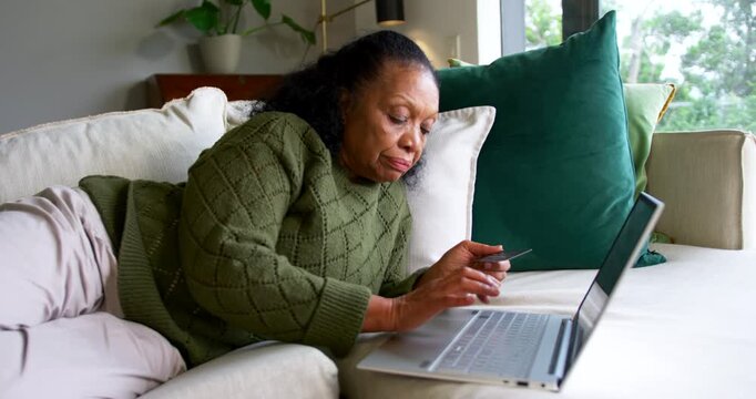Senior African American female holding credit card typing on laptop on couch entering payment info