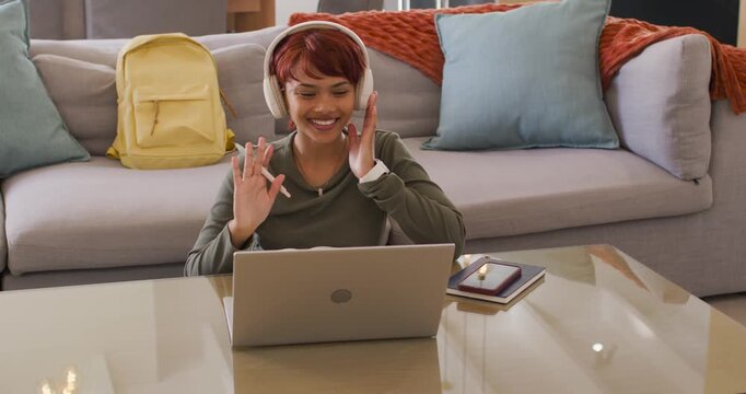 African American woman receiving invite adjusting headset waving at laptop noting stylus at home