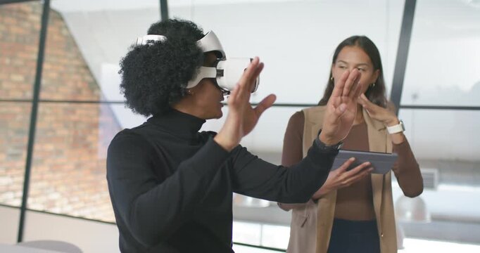 African American coworkers demoing VR after headset fitting in office, woman holding tablet guiding