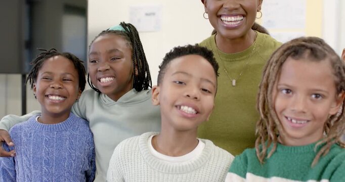 African American teacher with children posing for group portrait in classroom as camera tightening