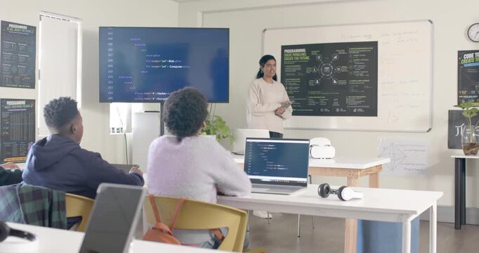 Indian lab teacher pointing at chart, teaching African American teens while screen showing code