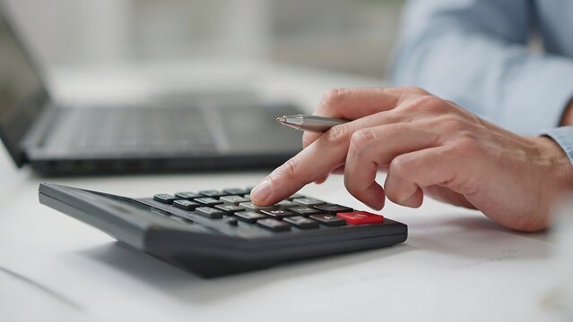 Financial analyst calculates figures on a desk with a calculator.