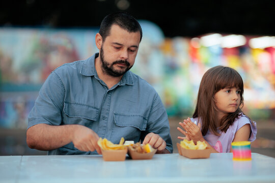 Happy Father And Little Daughter Eating Fish And Chips Together At Outdoor Fair. Dad and his young girl enjoying tasty street food seafood lunch at open air market tables