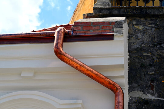 shiny new copper gutter, rain water leader, downspout or down pipe detail. home renovation and construction concept. textured white stucco exterior wall.