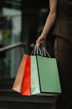 Close-up of a woman carrying colorful shopping bags outside a modern shopping mall, representing retail, consumer lifestyle, fashion, and successful shopping.
