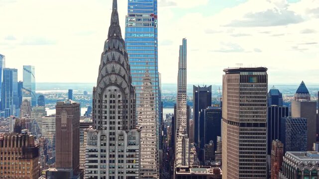Art deco skyscraper spire against glass tower, Manhattan, New York. Elevated perspective of historical stone facade, metal roof and cloudy sky.