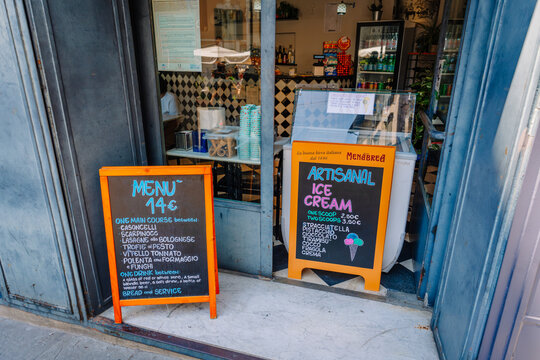 Authentic Bergamo stracciatella gelato displayed on an orange chalkboard sign outside a gelateria with a welcoming entrance