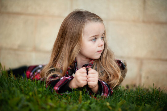 Pensive young girl in plaid coat lies on green grass