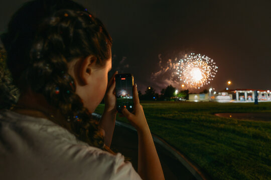 Young woman recording fireworks on her smartphone at night