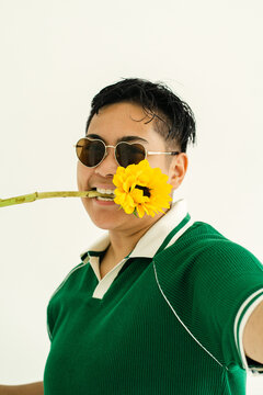 Androgynous person biting sunflower in heart sunglasses