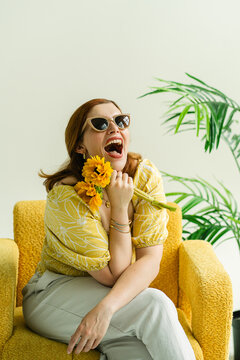 Joyful woman laughing with sunflowers in a yellow chair