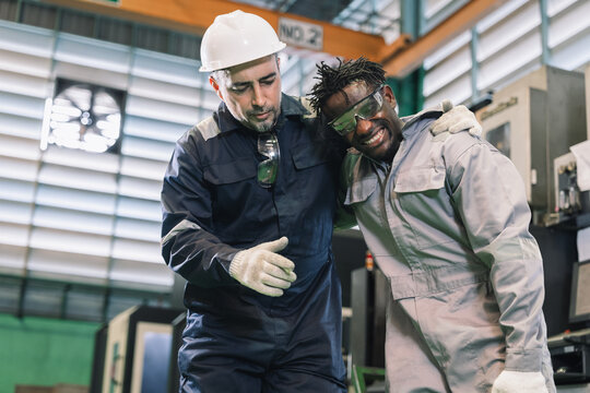 African engineer with hurting knee sitting on the floor and Caucasian worker in safety helmet helping and calling ambulance