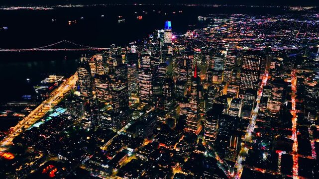 Above the illuminated San Francisco waterfront skyline, California. Drone view of Salesforce Tower, Bay Bridge lights and busy Embarcadero traffic at night.
