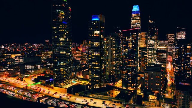Above illuminated towers along the Central Freeway, San Francisco, California. Aerial night view of Salesforce Tower, apartment high rises and dense highway traffic.