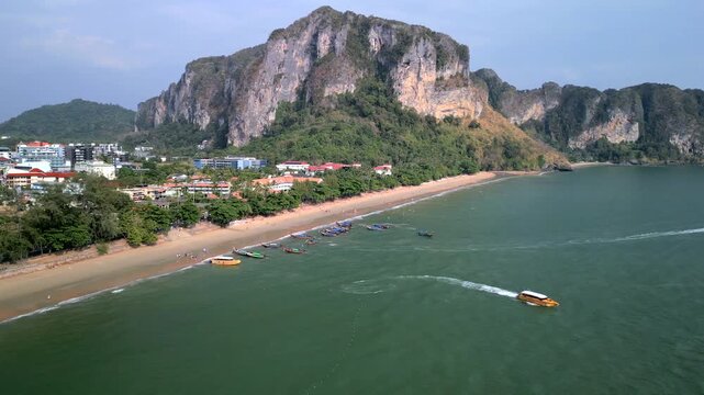 Aerial drone view of Ao Nang Beach in Krabi, Thailand. Tropical coastline with boats, sandy beach, turquoise sea, seaside resorts and lush limestone mountains in the background.