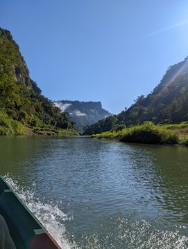 Scenic boat ride along Sangu River near Remakri in Bandarban, with water splash, misty green mountains, and blue sky.