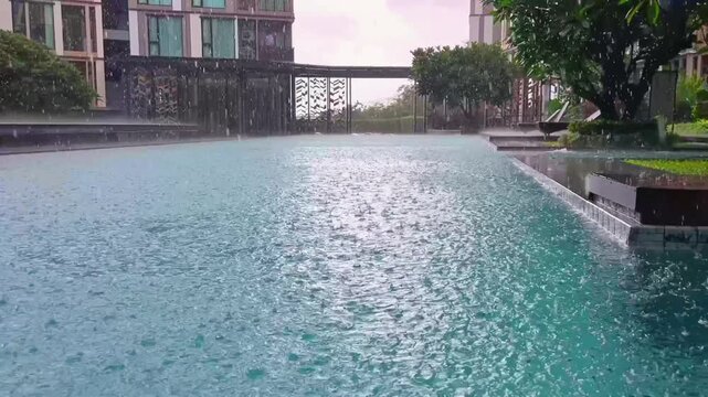 Heavy tropical rain creates dense ripples across the surface of a swimming pool at a modern residential complex in Phuket during Thailand's monsoon season.