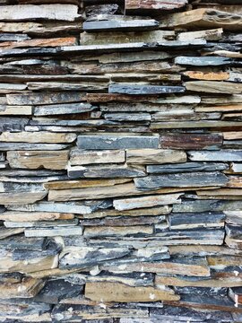 A rustic stacked slate wall showing varied colors and rough textures. Ideal for exterior design, stonework, and nature-inspired architecture conveying durability, rugged charm, and earthy appeal