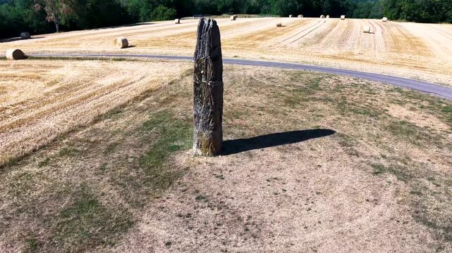 Pr&auml;historischer Gollenstein-Menhir auf einer Wiese bei sommerlicher Erntezeit mit Strohballen unter blauem Wolkenhimmel. Altes Kulturdenkmal in Mitteleuropa.