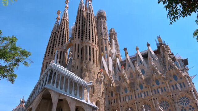Sagrada familia basilica exterior view under clear blue sky in barcelona spain cinematic tilt down.