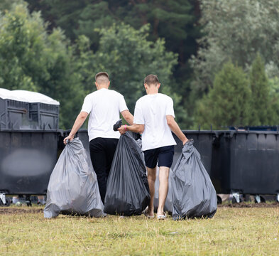 Two men carry large trash bags across a grassy field