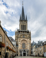 Naklejka premium Aachen Cathedral (Aachener Dom) low angle view framed by historic brick buildings under a cloudy sky in Aachen, Germany.