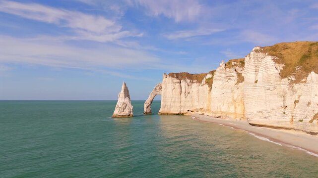 A low aerial shot captures a limestone arch and rock spire along the coast near Etretat, France.