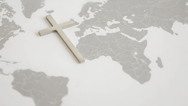Silver Christian cross lying on top of a gray world map background