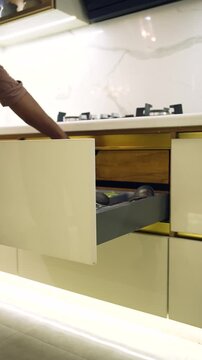 Modern kitchen drawer opening. Hand pulling out a sleek modular cabinet storage unit.