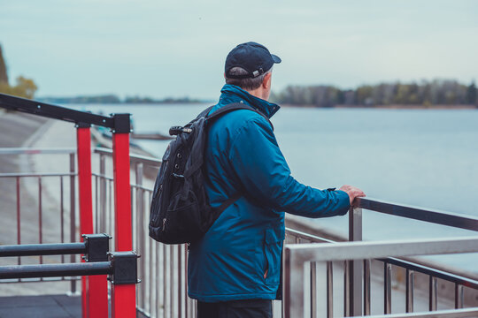 Thoughtful senior man aged 50s 60s in blue jacket and cap standing alone outdoors looking into distance, psychological mental health concept of loneliness and reflection