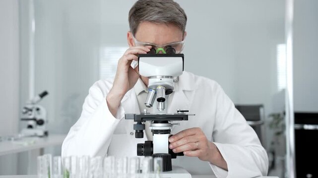 Research scientist looking through a microscope. Adjusting the focus and objective to analyze a specimen