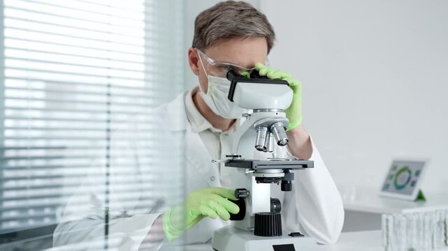 Research scientist looking through a microscope. Adjusting the focus and objective to analyze a specimen