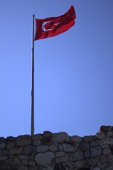 Fototapeta premium Waving Turkish Flag on Historic Castle Walls Against Clear Blue Sky